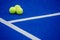 Three paddle tennis balls on a blue synthetic grass paddle tennis court surface