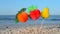 Three paper fruits on stick stand on sandy beach near sea on sunny summer day.