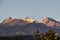 Three peaks of the mountains of the Zailiysky Alatau meet the summer sunrise above the spruce thickets.