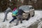 Three people push a car that is stuck in deep snow