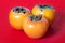 Three persimmons on red background