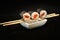 Three pieces of syake maki roll lying on sticks on a black background.