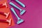 Three pink plastic razors against blue ones on a red-pink background