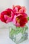 Three pink tulips in a cubic glass vase on a white background