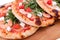 Three pizzas with prawns, tomatoes, arugula and cheese on a wooden background