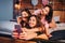 Three playful young women taking selfie on bed in room. Two models play with hair of third girl. They look on camera