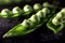 Three pods with peas covered with drops of water on dark table surface.