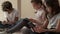 Three pretty multi ethnic african, caucasian and korean little kids sit indoors using wireless gadgets. Overuse of modern tech