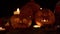 Three pumpkins with faces on Halloween with candles inside flickering in dark