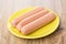 Three raw peeled sausages in yellow saucer on table