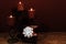 Three red candles in metal holders and red rose, present with white bow on wooden table.