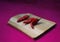 Three red hot peppers on board in still life, diagonal view, with magenta background