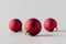 Three red matte Christmas balls on a seamless grey background