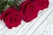 Three red roses on white wooden background.