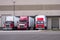 Three red semi trucks are among the dock for loading trailers