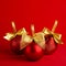 Three red shiny christmas balls with gold shimmer bow on bright deep red background, square, closeup. New year background.
