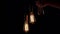 Three retro lamps hang on black background. Antique bulbs with old lamp holder are switched on sequentially by male hand