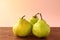 Three ripe, fresh, organic Green Anjou pears with the stems on a dark wooden table against bright pink background and sun light.