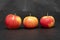 Three ripe fresh organic sweet red apples with yellow spots, closeup, on black background