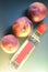 Three ripe peaches close-up over a bottle with a pink label on an embossed leathery azure green background