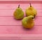 Three ripe yellow pears are on a pink wooden tray.