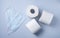 Three rolls of white toilet paper and face masks on a blue background. Pandemic, covid-19, essential goods, scarcity