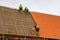 Three roofers in protective workwear installing new clay tiles, new clay tiles layer covering