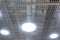 Three round LED lighting lamps on the ceiling of a commercial building. The mesh suspended ceiling creates a beautiful