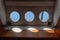 Three round portholes seen from inside a ship looking out on the ship`s rigging and blue sky