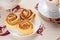 Three ruddy buns on a white saucer with herbal apple tea in a cup and a teapot in the background.