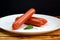 Three sausages lie on a white plate stacked in a pile