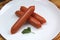 Three sausages lie on a white plate stacked in a pile