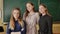 Three schoolgirls positively posing in front of the camera on the background of a school board