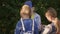 Three schoolgirls standing and talking on green bush background in park