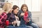 Three shocked female friends with coffee and smartphone at home