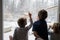 Three siblings, brothers and sister, looking out the window amazed by the snowy winter nature