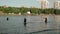 Three silhouettes of unrecognisable men in pond of city park playing with small ball