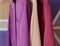 Three silk dresses hung on an offinger in the colors of magenta, fuchsia, violet, pink, poweder pink, peach pink, coral pink, rose