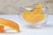 Three slices of orange in a transparent bowl with orange peel next to it