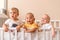 Three small funny babies are standing in the crib