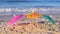 Three small paper cocktail umbrellas stand in sand on sandy beach close-up.