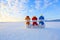 Three small snowman in colorful hats are standing on the snow. The scenery with mountains, field in snow, blue sky.