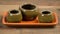 three small vases sitting on a tray on a wooden table, one of them is green and the other is brown with a brown base