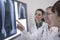 Three smiling doctors looking at x-rays of human bones, one doctor is pointing