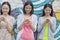 Three smiling young woman standing side by side and texting on their phones in front of a wall with graffiti