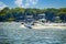 Three speedboats at lake racing in choppy water past lakeside homes and trees on nearby shore on sunny day - selective focus