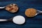 Three spoons with cane sugar, brown sugar cubes and white sugar side by side on a blue wooden board. Comparison of sugars