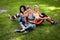 Three sportive female friends sitting on a grass at the park outdoors, make selfie on a phone with a stick