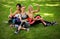 Three sportive female friends sitting on a grass at the park outdoors, make selfie on a phone with a stick