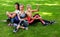 Three sportive female friends sitting on a grass at the park outdoors, make selfie on a phone with a stick